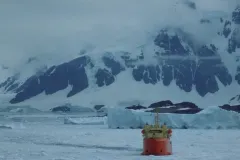 A large red research vessel among icy waters and snowy mountains
