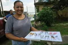 A woman stands holding a white tray that displays lionfish jewelry.