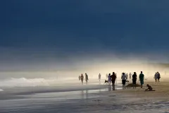 A beach scene with groups of people walking in the water and playing with the sand.