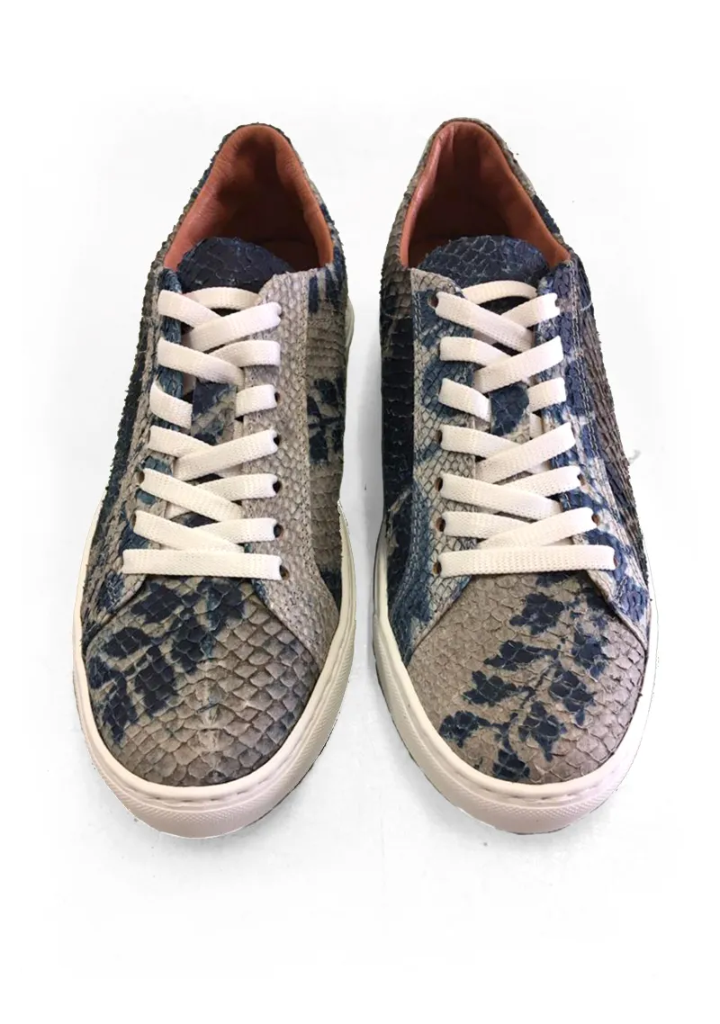 A pair of silver colored sneakers with white shoelaces, made from fish skin and dyed with blue floral patterns.