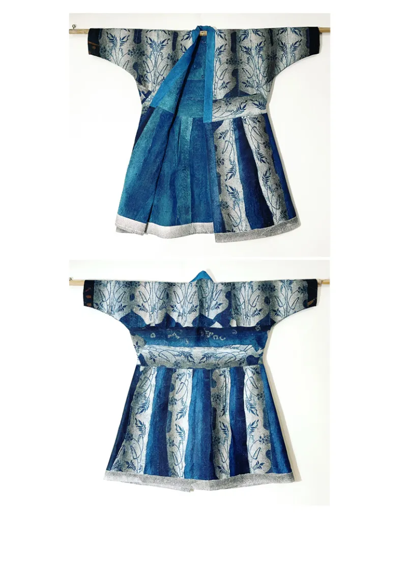A blue, silver, and black fish skin robe displayed hanging from a rod. The robe is created from multiple fish skin sewn together and dyed with indigo.