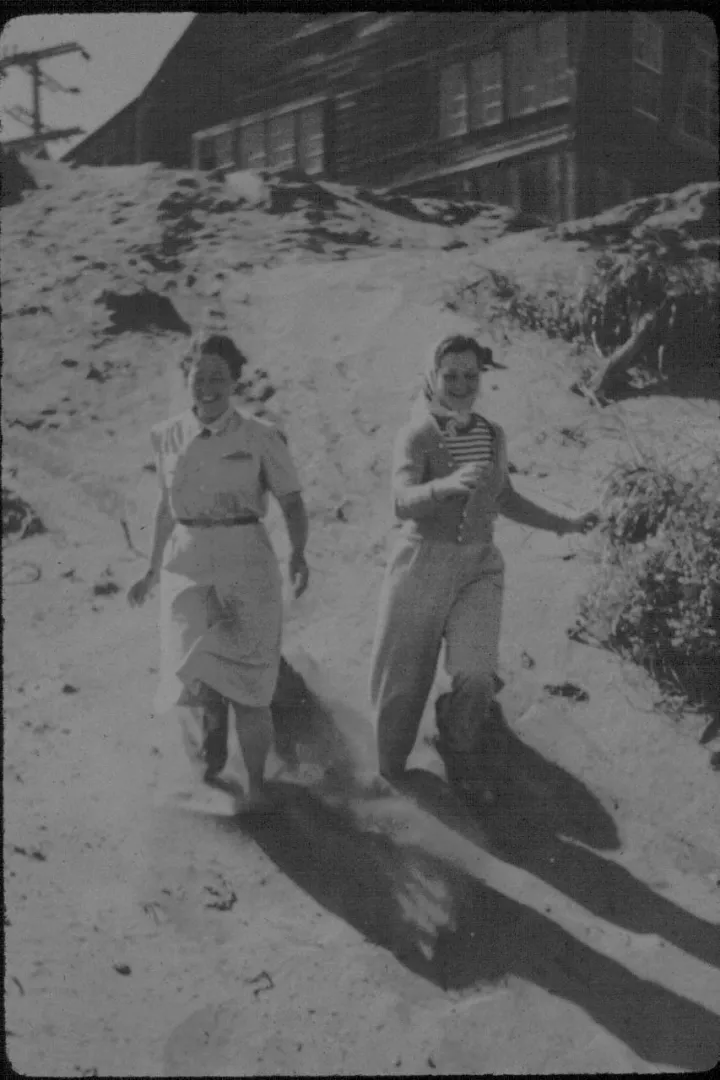 two young women gleefully race down a sandy hill